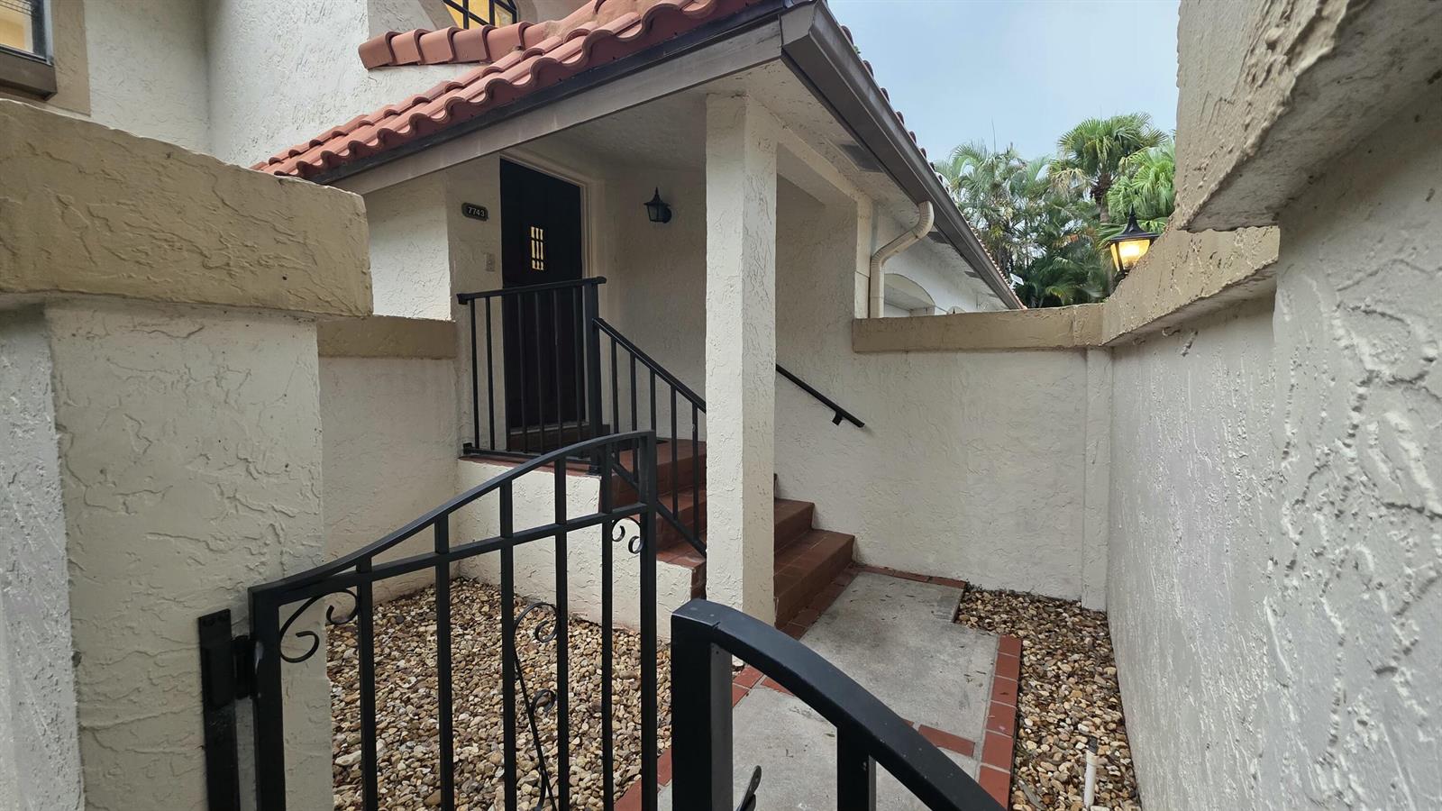 An exterior view of a home entrance with a gated courtyard, stairs, and tiled roof — 7743 La Mirada Drive, Boca Raton FL 33433, BOCA RATON, FL