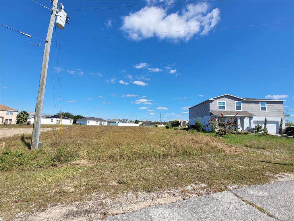 A vacant, grassy lot sits next to a two-story house under a blue sky — 2233 PECOS COURT, KISSIMMEE, FL