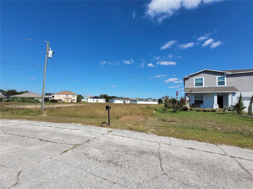 A vacant, grassy residential lot sits next to a two-story house under a blue sky — 2233 PECOS COURT, KISSIMMEE, FL
