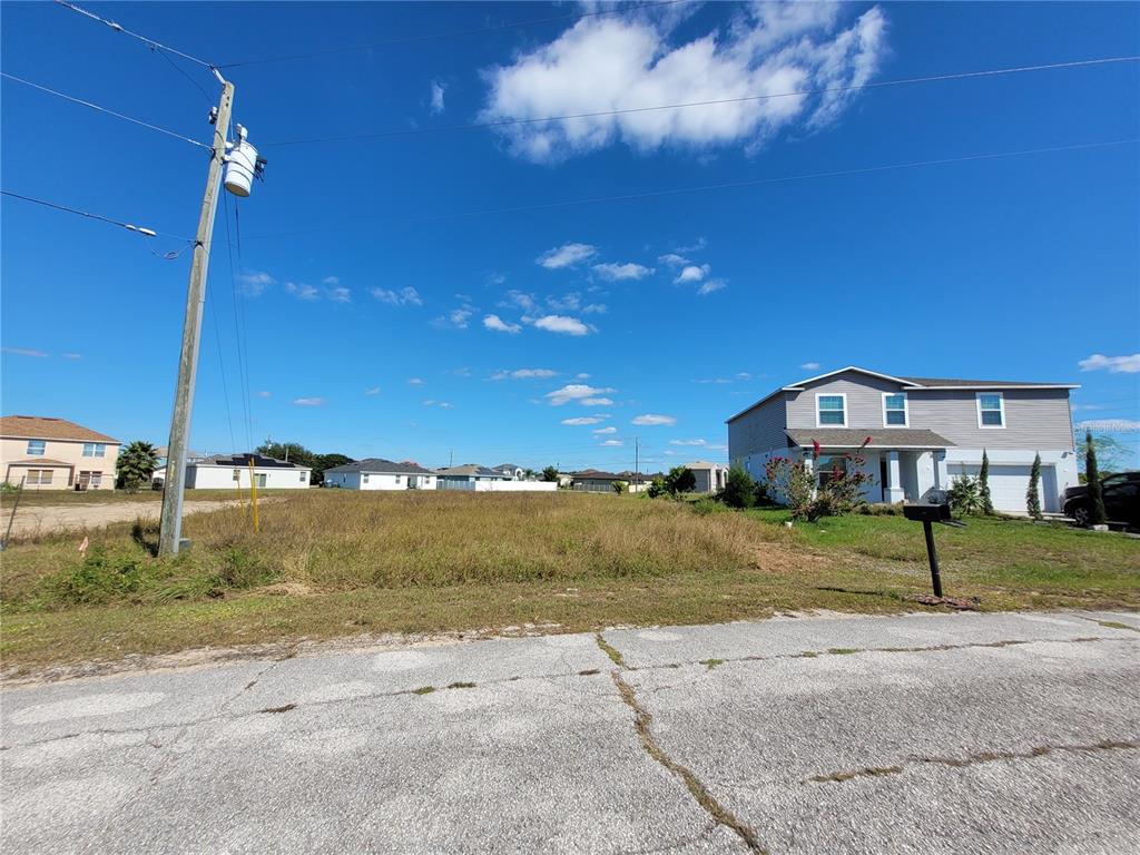 A vacant, grassy residential lot sits between two houses under a clear blue sky — 2233 PECOS COURT, KISSIMMEE, FL