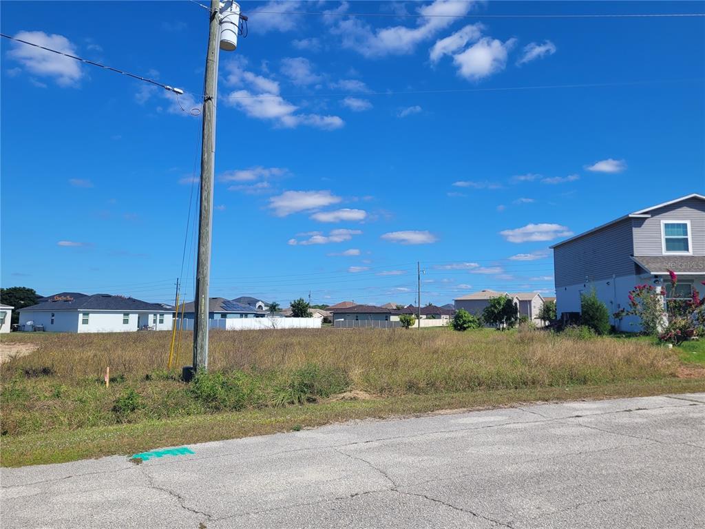 A vacant, grassy residential lot sits next to a two-story house under a blue sky — 2233 PECOS COURT, KISSIMMEE, FL