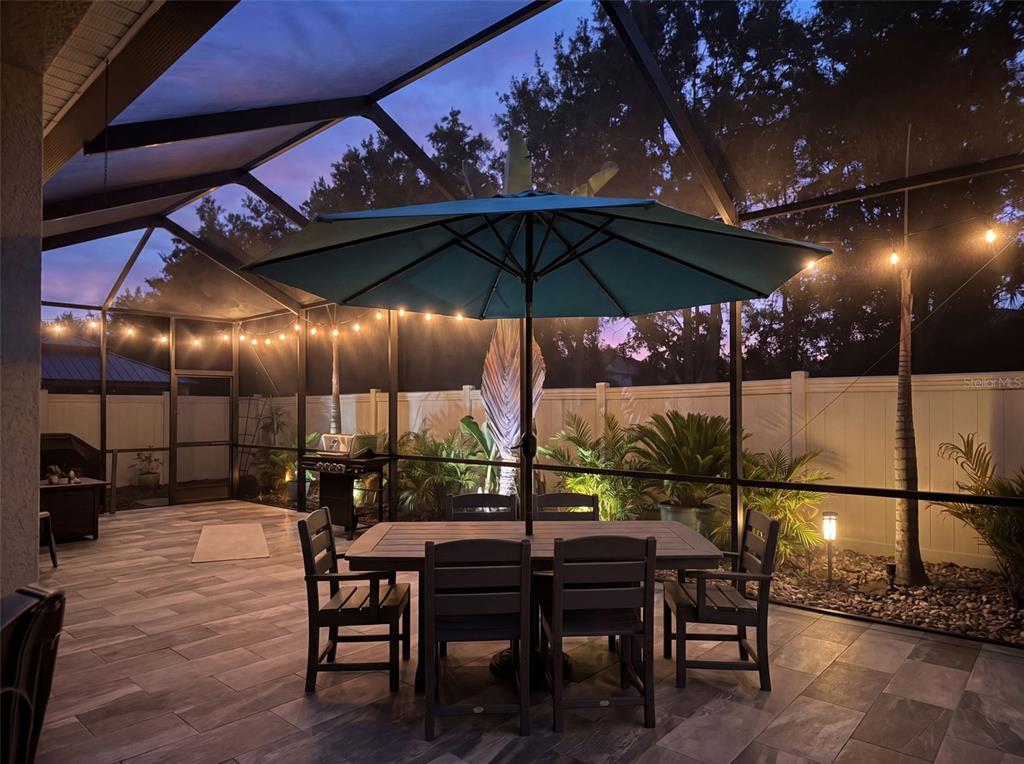 A screened-in patio features gray tile flooring, a dining set, and a blue umbrella — 31486 TANSY BEND, WESLEY CHAPEL, FL