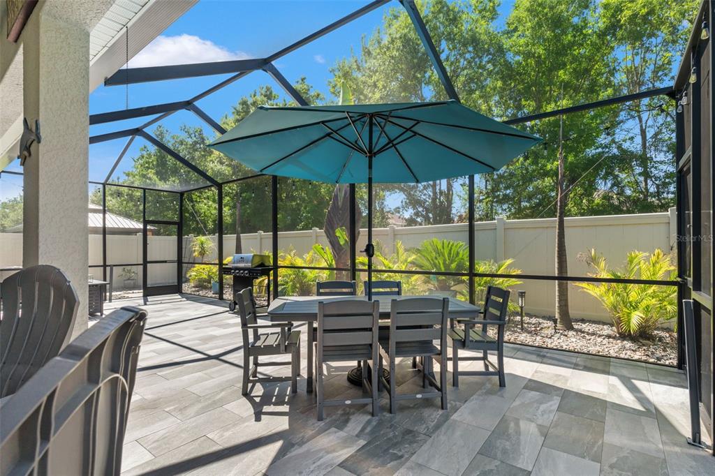 A screened-in patio features a dining set, a grill, and tile flooring — 31486 TANSY BEND, WESLEY CHAPEL, FL