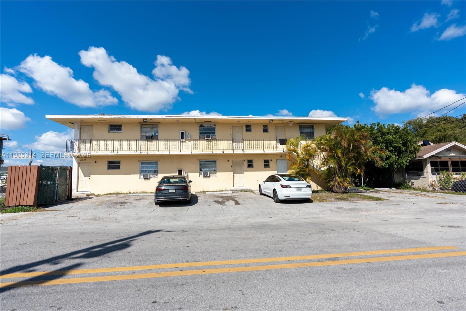 A two-story, light-yellow apartment building features a balcony and a paved parking lot — 6401 NW 12th Ave, Miami FL 33150, MIAMI, FL