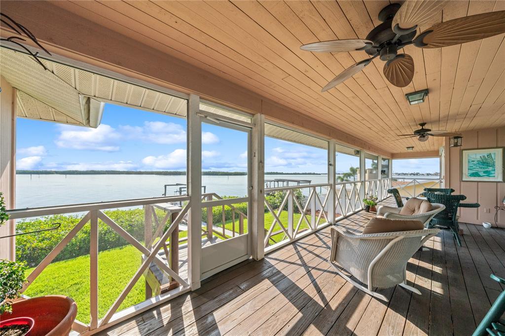 A screened-in wooden porch overlooks a body of water with outdoor seating and ceiling fans — 6663 BAYOU GRANDE BOULEVARD NE, ST PETERSBURG, FL