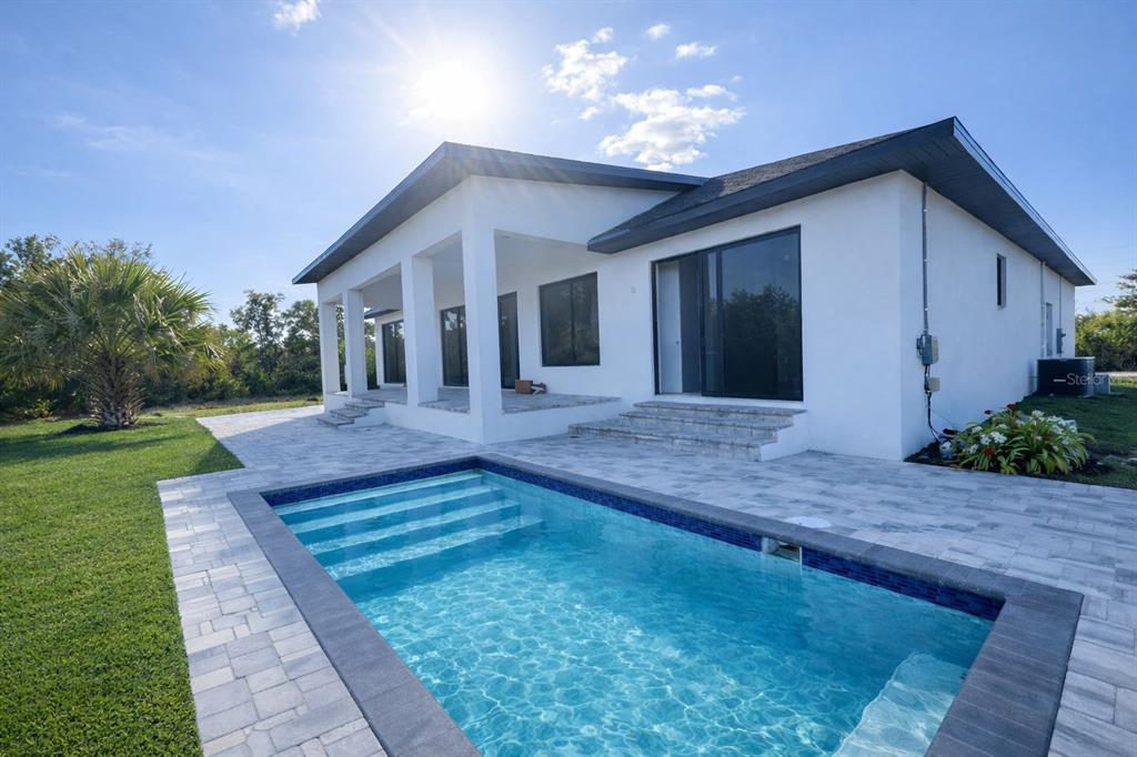A modern white house with a swimming pool and stone patio under a sunny sky — 9477 ATTICA CIRCLE, PORT CHARLOTTE, FL