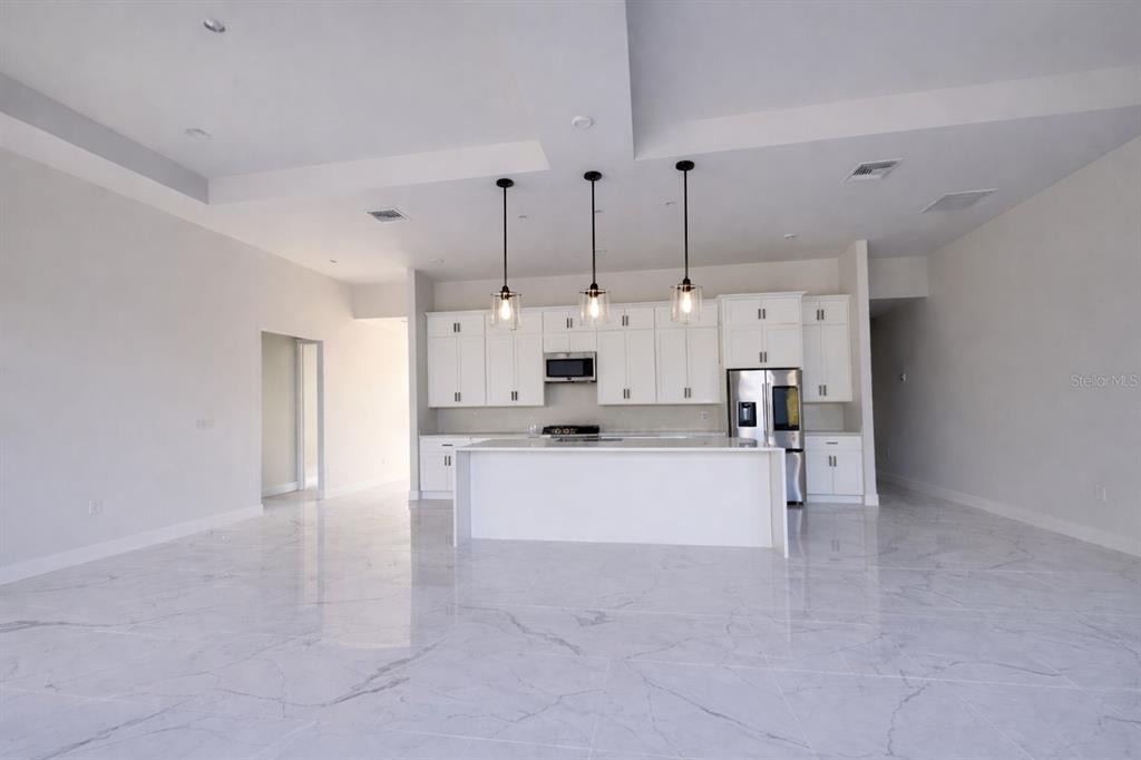 A modern kitchen features white cabinetry, a central island, and light-colored marble-style tile flooring — 9477 ATTICA CIRCLE, PORT CHARLOTTE, FL