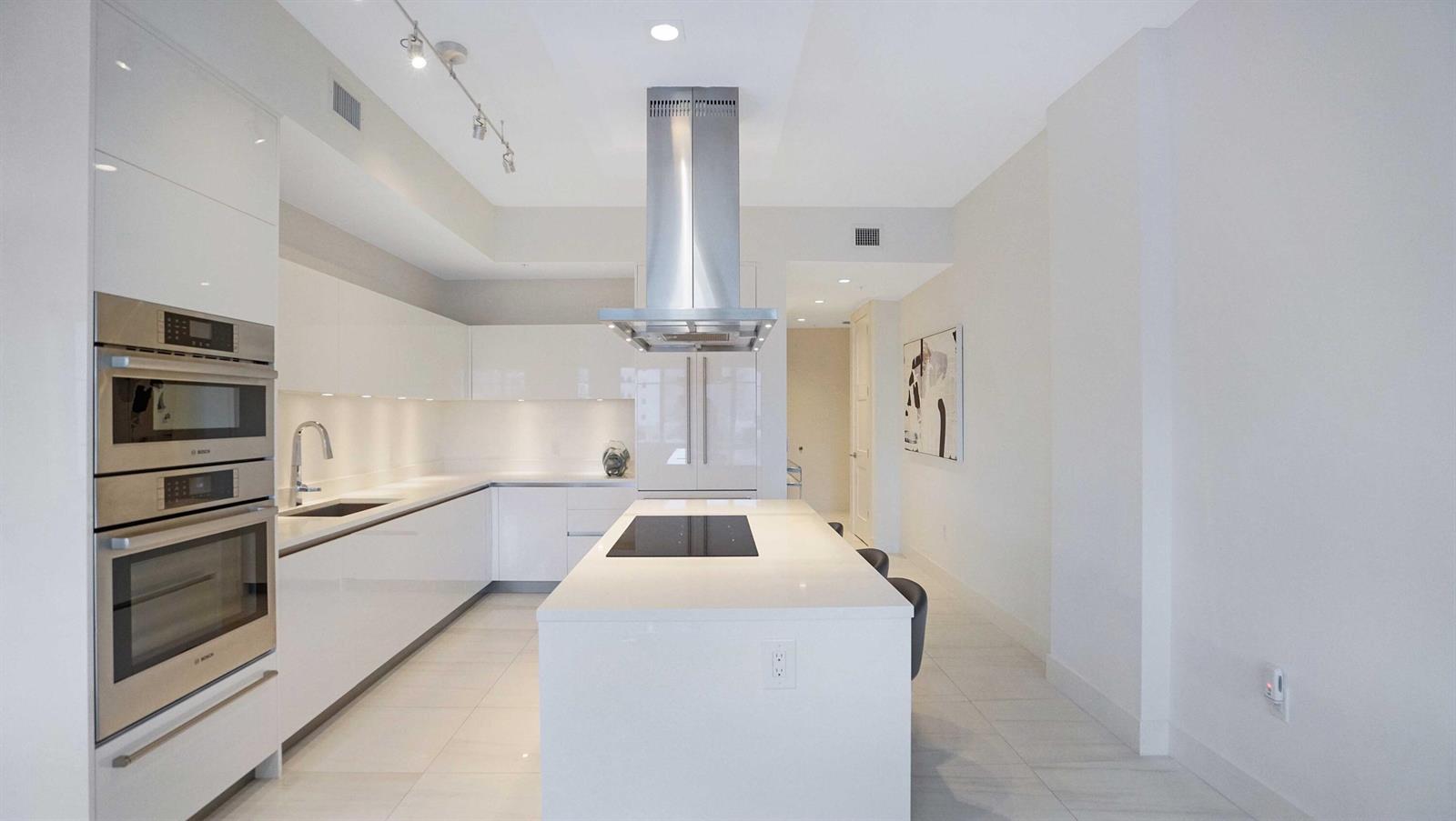 A modern white kitchen features a central island with a cooktop and stainless steel appliances — 155 E Boca Raton Road # 501, Boca Raton FL 33432, BOCA RATON, FL