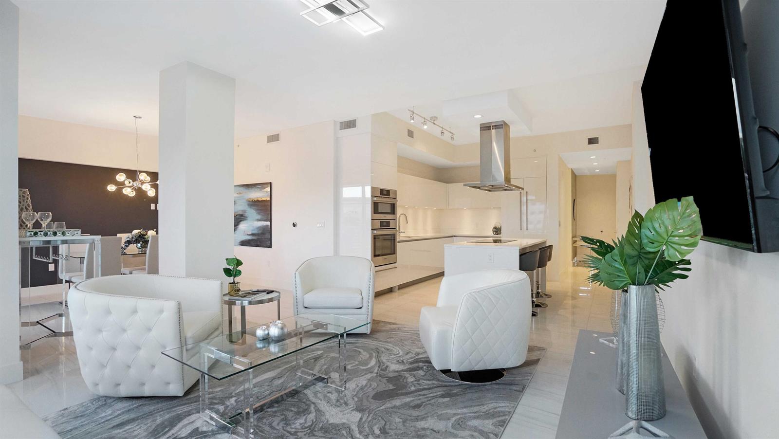 A modern open-concept living room features white tufted armchairs, a glass coffee table, and kitchen — 155 E Boca Raton Road # 501, Boca Raton FL 33432, BOCA RATON, FL