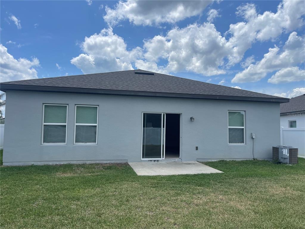 The back exterior of a grey house features a concrete patio and sliding glass doors — 2858 NEVERLAND DRIVE, NEW SMYRNA BEACH, FL