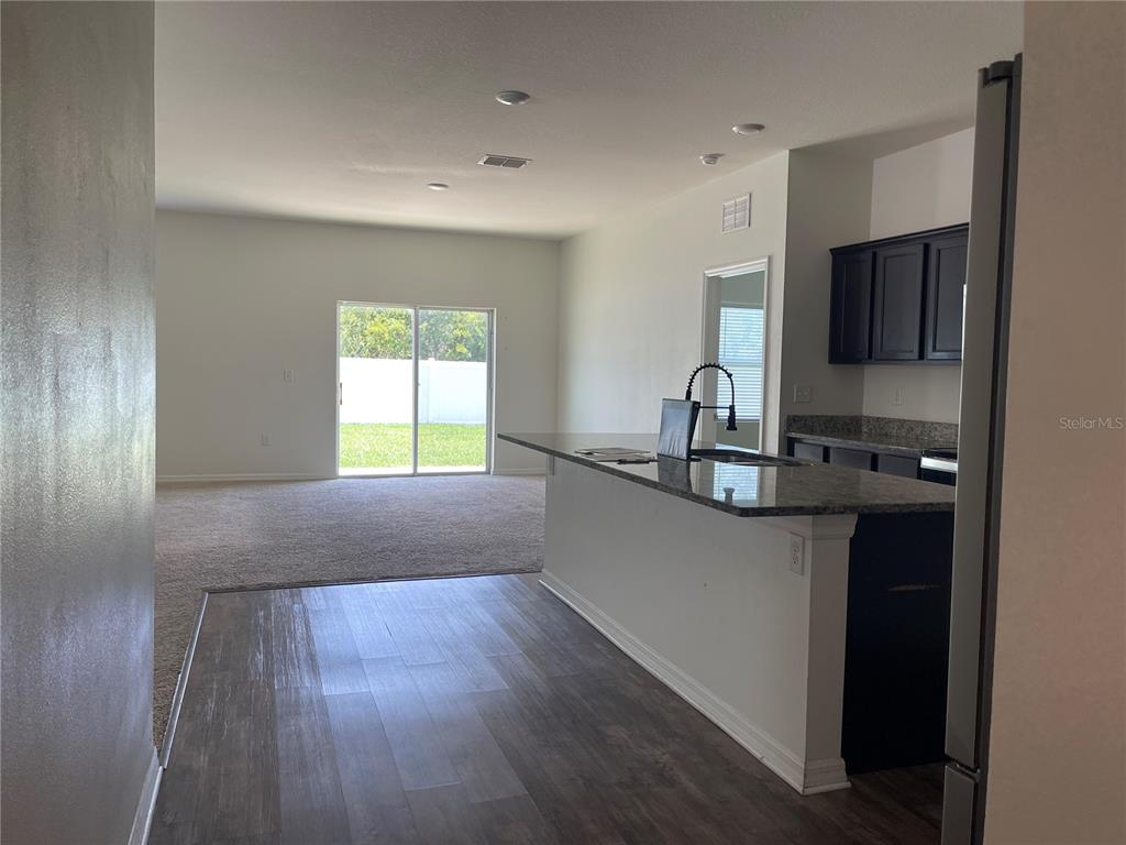 A kitchen with dark cabinets and a granite island overlooks a carpeted living area — 2858 NEVERLAND DRIVE, NEW SMYRNA BEACH, FL
