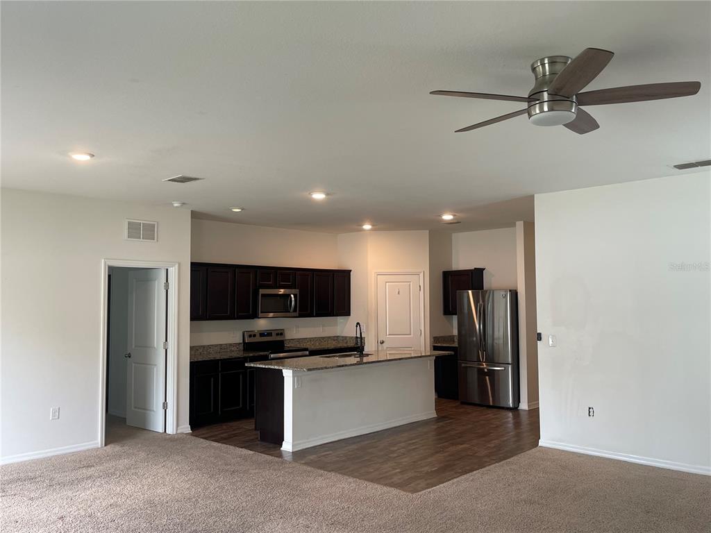 An open-concept kitchen features dark cabinetry, granite countertops, stainless steel appliances, and a center island — 2858 NEVERLAND DRIVE, NEW SMYRNA BEACH, FL
