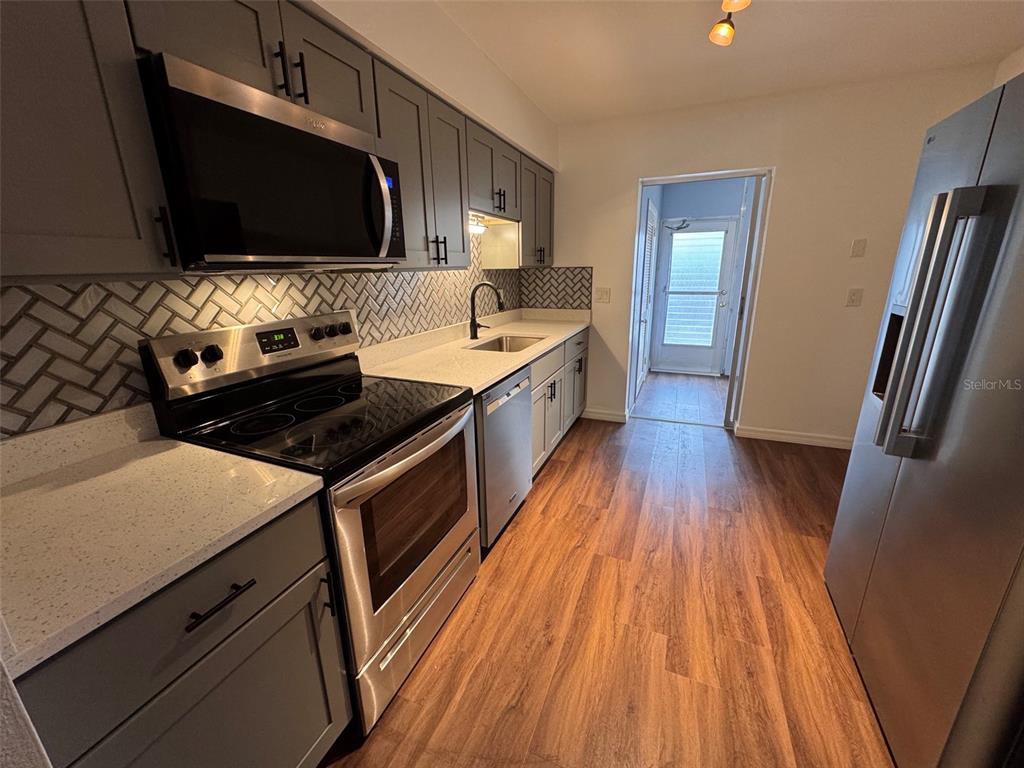 A galley kitchen features gray cabinets, stainless steel appliances, and a herringbone tile backsplash — 5155 9TH AVENUE N UNIT 104, ST PETERSBURG, FL