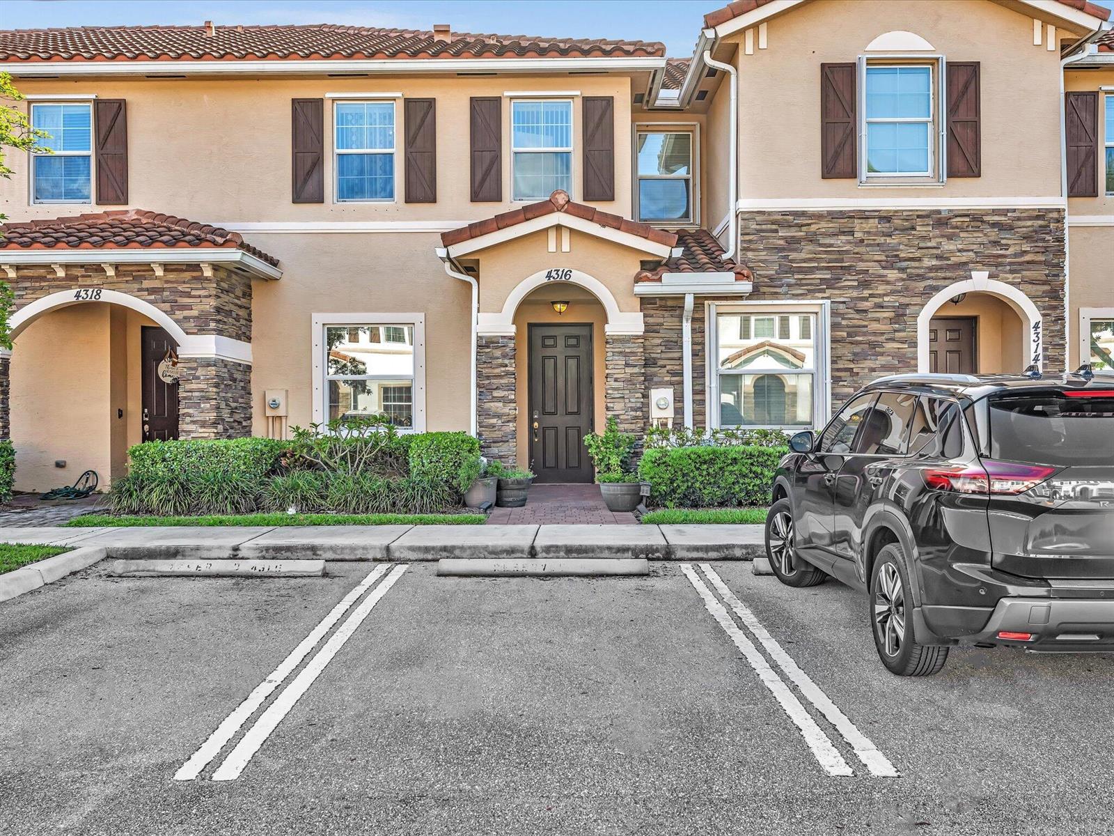 A two-story townhouse exterior features a stone facade, brown shutters, and a paved parking area — 4316 Maybelle Lane, West Palm Beach FL 33417, WEST PALM BEACH, FL