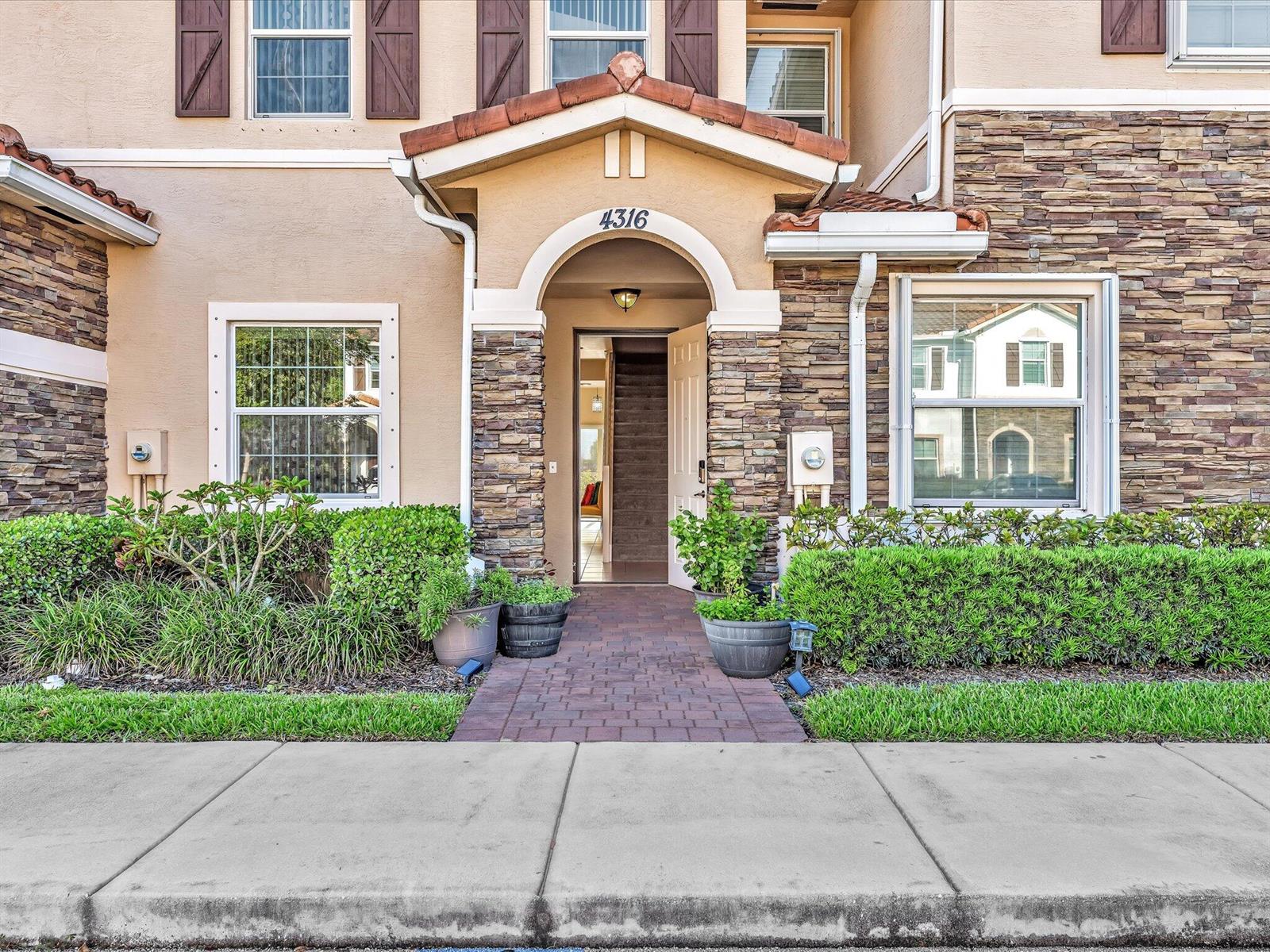 The exterior of a two-story townhouse features a stone facade, arched entryway, and landscaped garden — 4316 Maybelle Lane, West Palm Beach FL 33417, WEST PALM BEACH, FL