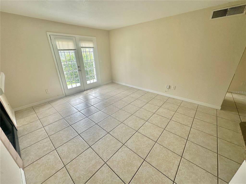 An empty room features beige tile flooring, light-colored walls, and a set of French doors — 2550 N ALAFAYA TRAIL UNIT 2209, ORLANDO, FL