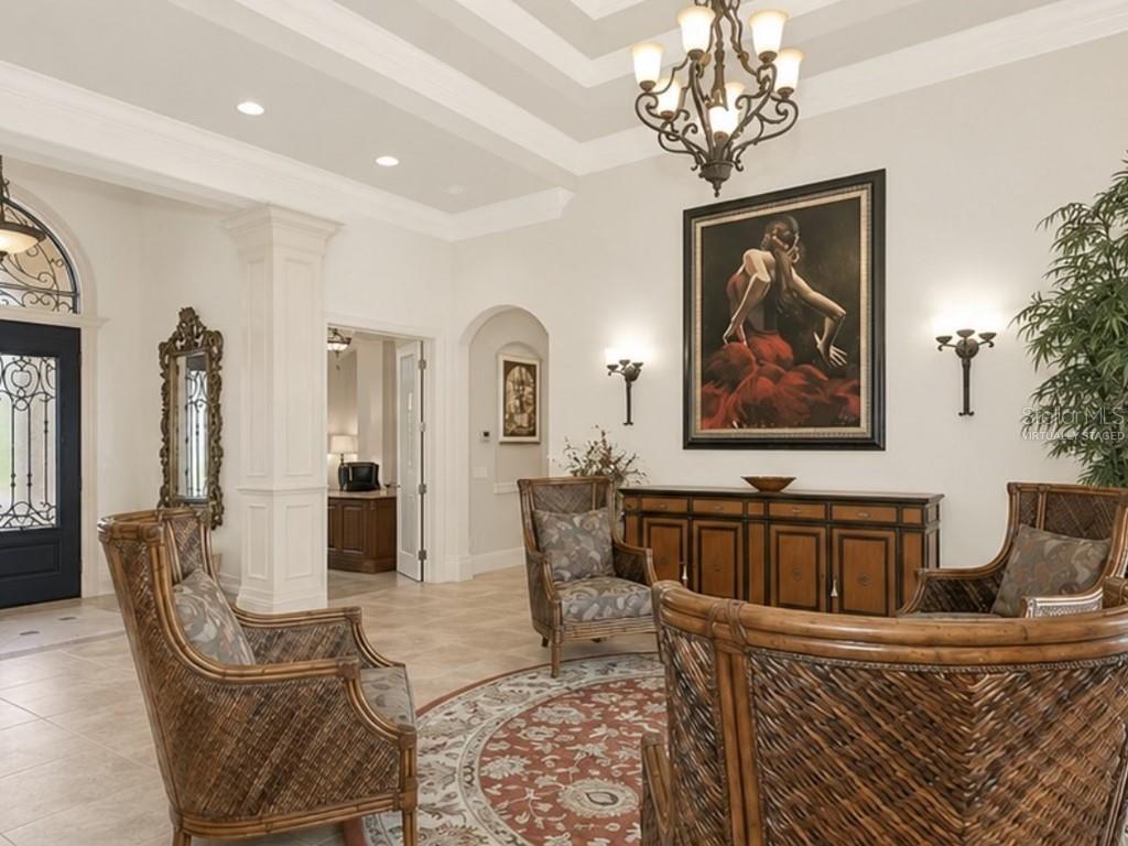 A spacious foyer features tile flooring, a chandelier, wicker armchairs, and a large framed painting — 8305 FARINGTON COURT, BRADENTON, FL