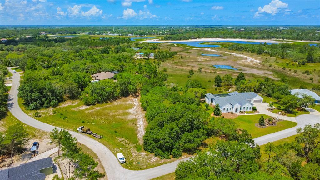 An aerial view shows a residential neighborhood with houses, wooded areas, and a small lake — 10446 SCENIC LAKE DRIVE, WEEKI WACHEE, FL
