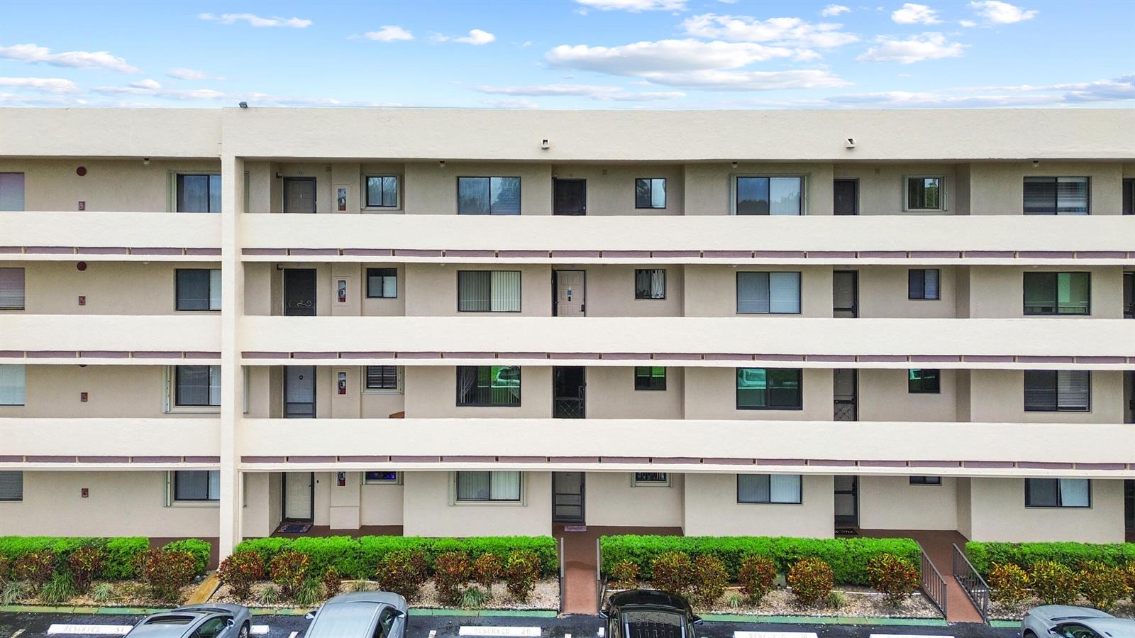 A four-story apartment building exterior features beige walls, horizontal balconies, and a landscaped ground level — 3154 Via Poinciana # 412, FL 33467, FL