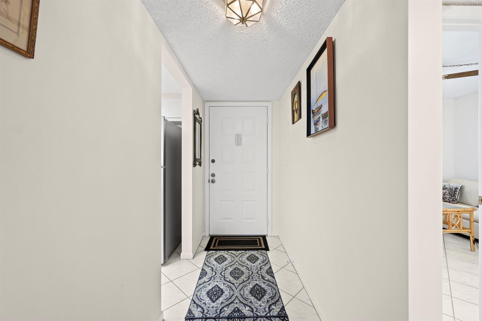 A white-walled entryway features a front door, tile flooring, and a patterned runner rug — 3154 Via Poinciana # 412, FL 33467, FL