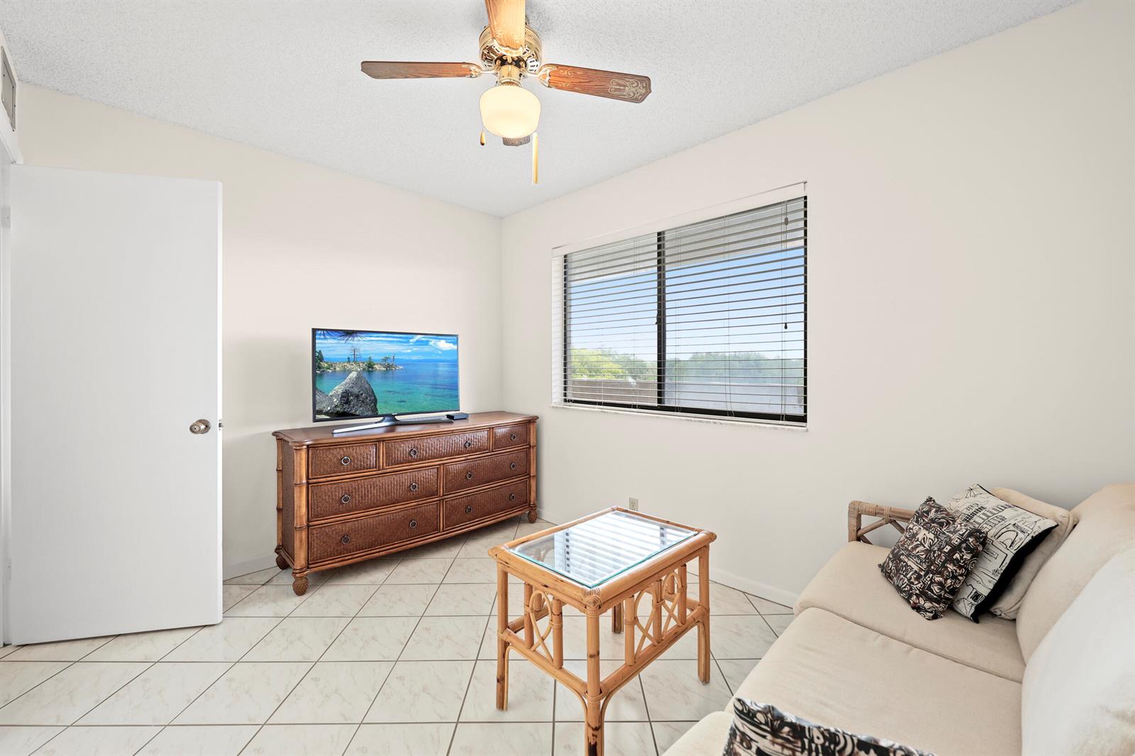 A bedroom features a wicker dresser, a glass-topped table, a sofa, and tile flooring — 3154 Via Poinciana # 412, FL 33467, FL