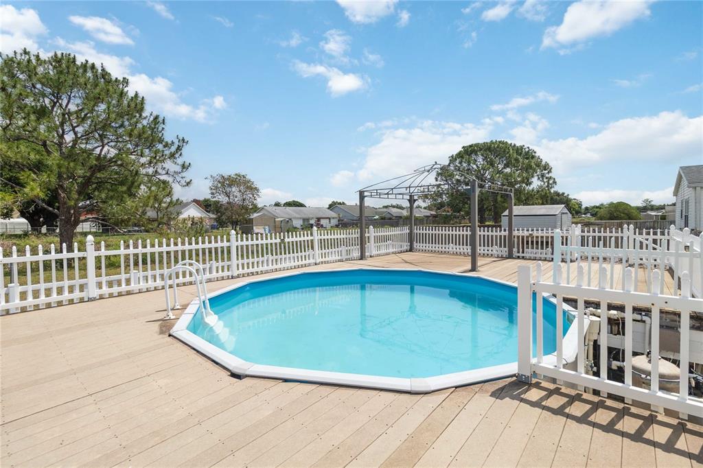 An above-ground swimming pool sits on a wooden deck enclosed by a white picket fence — 2030 CRYSTAL LANE, ST CLOUD, FL