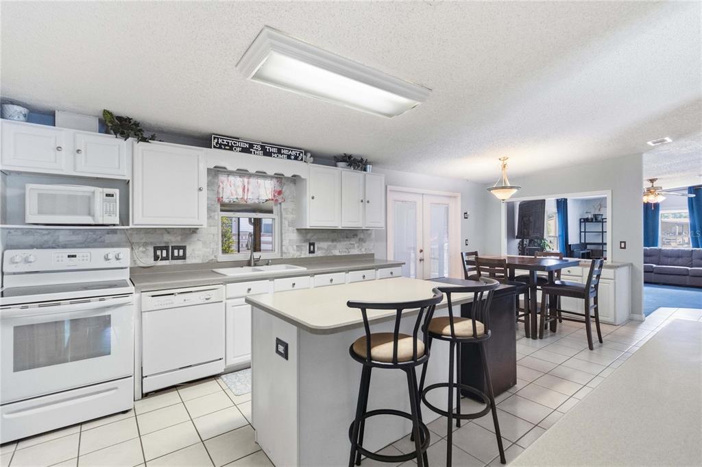 A kitchen with white cabinets, a central island with bar stools, and tiled flooring — 2030 CRYSTAL LANE, ST CLOUD, FL