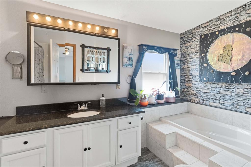 A bathroom features a white vanity, a large mirror with lights, and a stone-accented tub — 2030 CRYSTAL LANE, ST CLOUD, FL