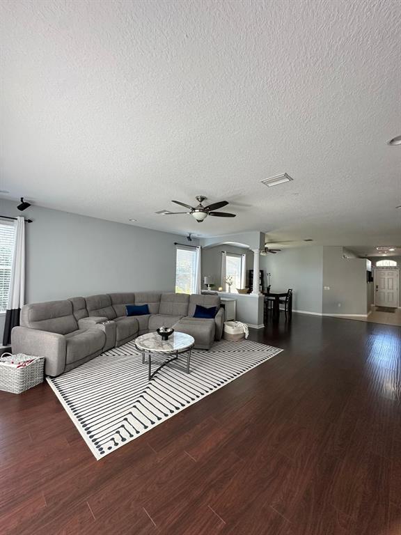 A spacious living room features a large gray sectional, patterned rug, and dark wood flooring — 32029 GARDEN ALCOVE LOOP, WESLEY CHAPEL, FL