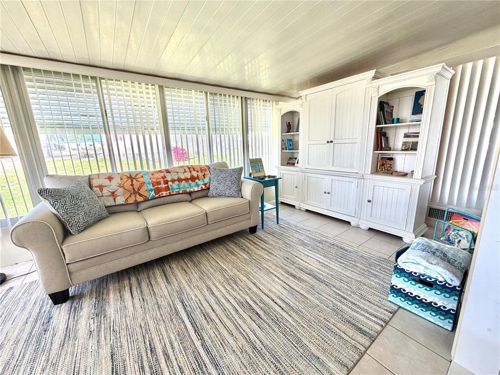 A sunroom features a beige sofa, a large white entertainment center, and a striped rug — 408 PALO VERDE DRIVE, LEESBURG, FL