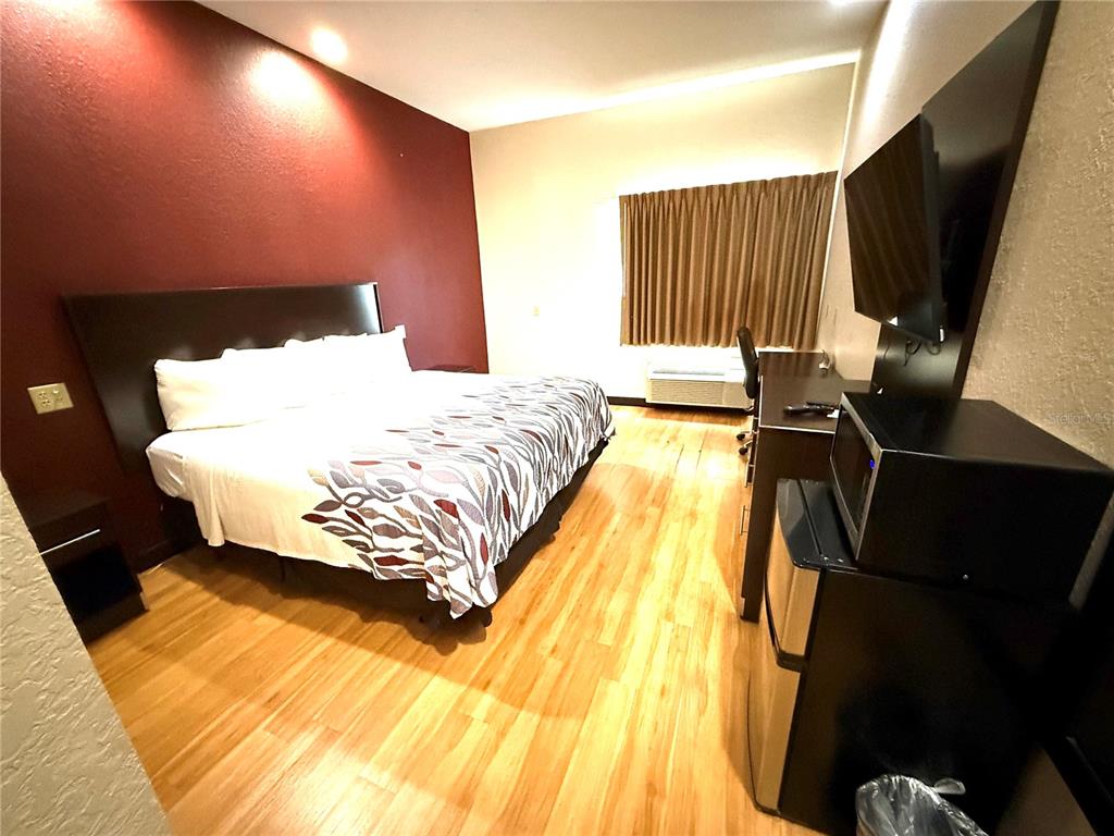 A hotel room features a bed with a patterned cover, wood flooring, and a desk — 120 NW 40TH AVENUE, OCALA, FL