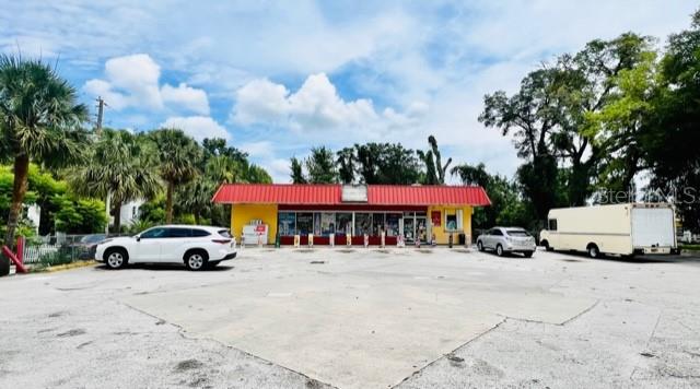 A commercial building with a red metal roof sits behind a large paved parking lot — 223 E VOORHIS AVENUE, DELAND, FL