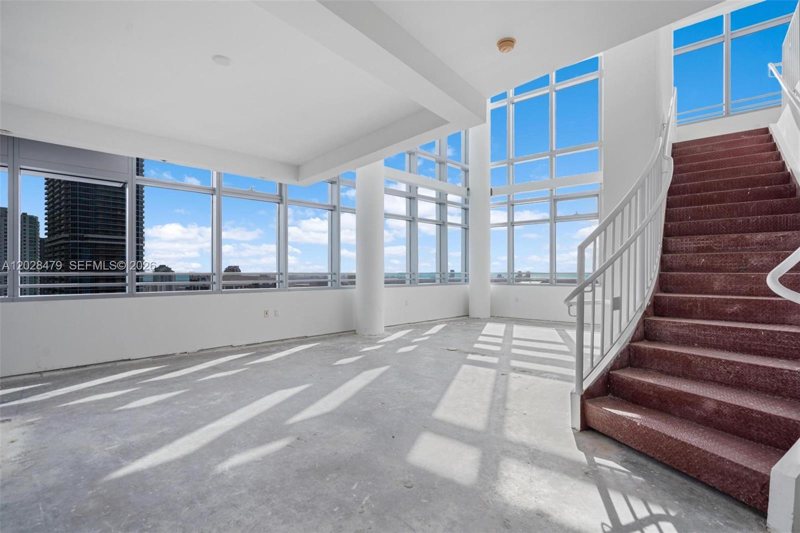 An empty room features floor-to-ceiling windows, concrete flooring, and a red metal staircase — 1395 Brickell Ave # 3410, Miami FL 33131, MIAMI, FL