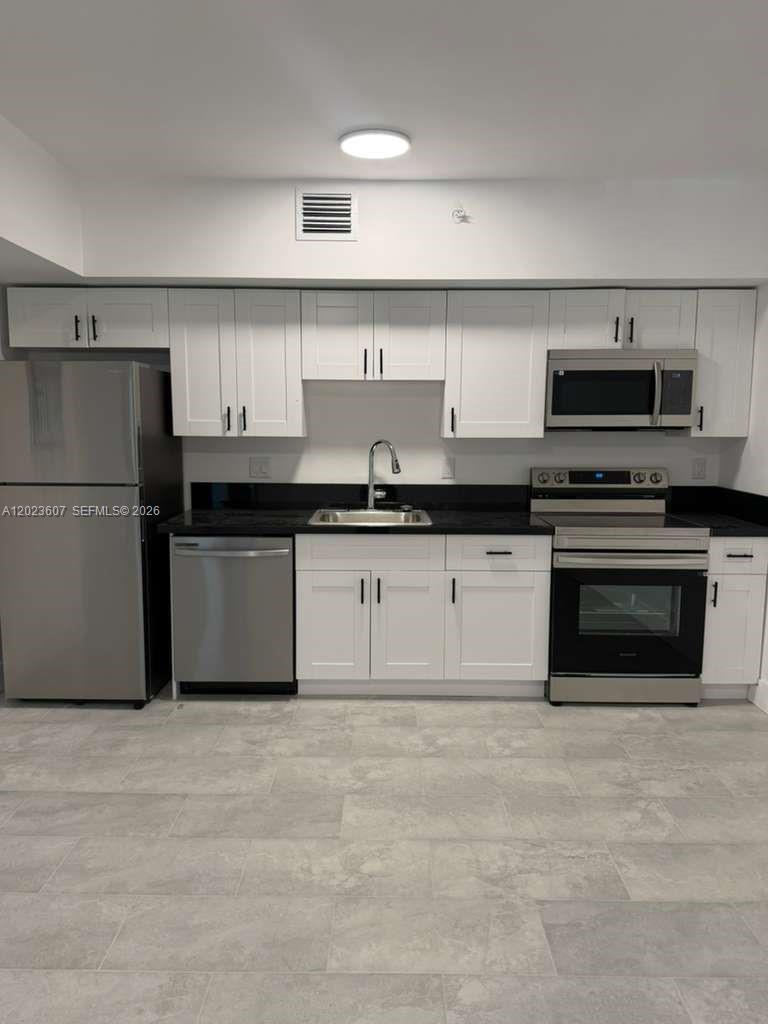 A kitchen features white cabinets, stainless steel appliances, and black countertops over gray tile flooring — 147 Nw 59th St # 203, Miami FL 33127, MIAMI, FL
