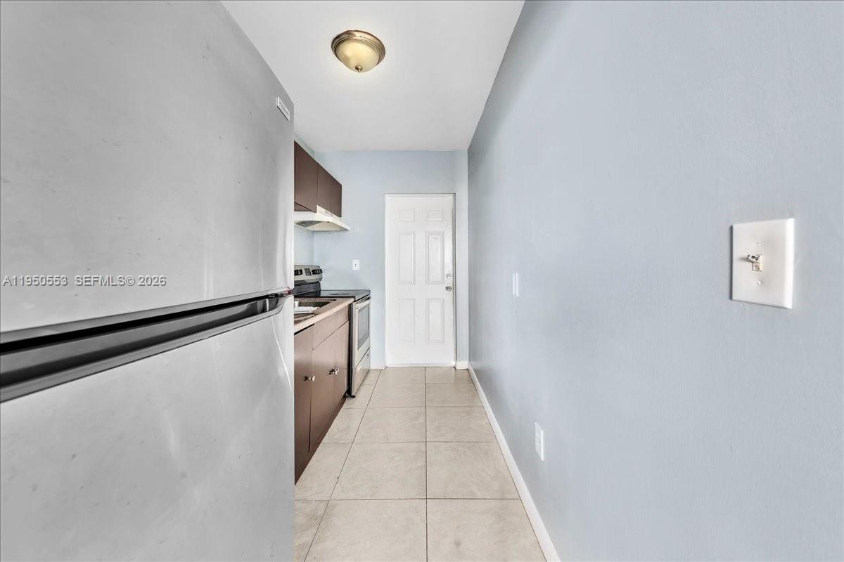 A narrow kitchen features stainless steel appliances, dark wood cabinets, and light tile flooring — 365 NW 8th St # 202, Miami FL 33136, MIAMI, FL