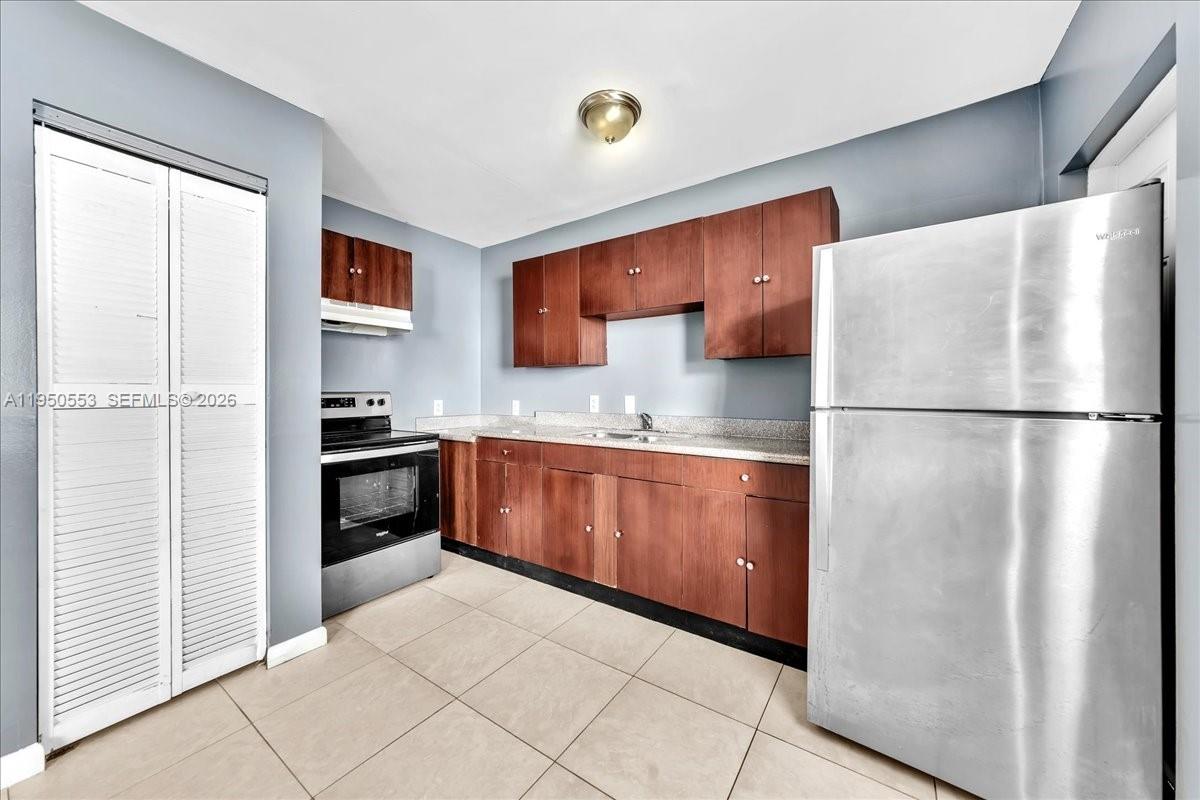 A kitchen features wood cabinets, stainless steel appliances, light countertops, and beige tiled flooring — 365 NW 8th St # 202, Miami FL 33136, MIAMI, FL