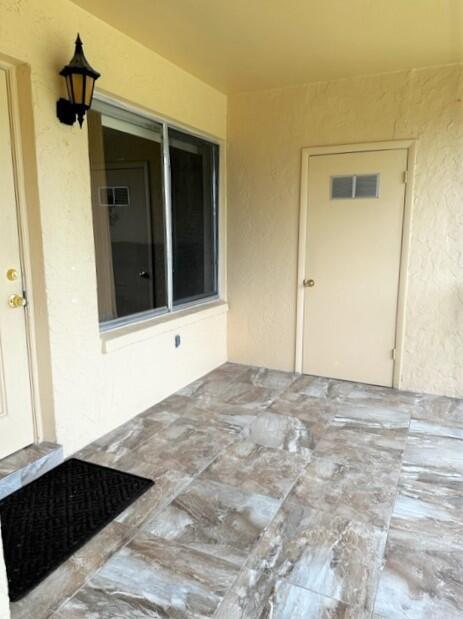 A covered patio with light-colored walls, a large window, a utility door, and tiled flooring — 441 Pine Glen Lane # 2, FL 33463, FL