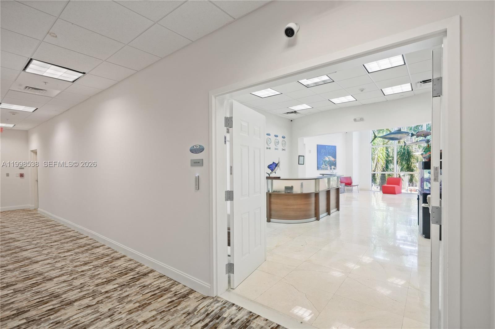 A hallway with patterned carpet leads into an office reception area with tile flooring — FORT LAUDERDALE, FL
