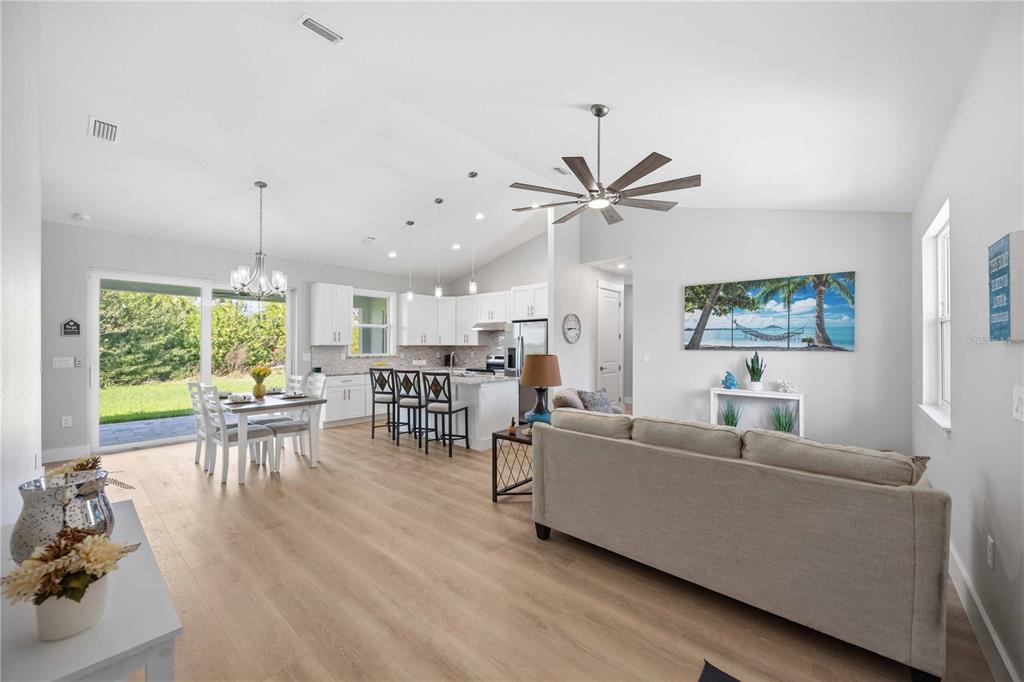 An open-concept living and dining area features light wood flooring, white cabinetry, and a ceiling fan — 10443 RIVERSIDE ROAD, PORT CHARLOTTE, FL
