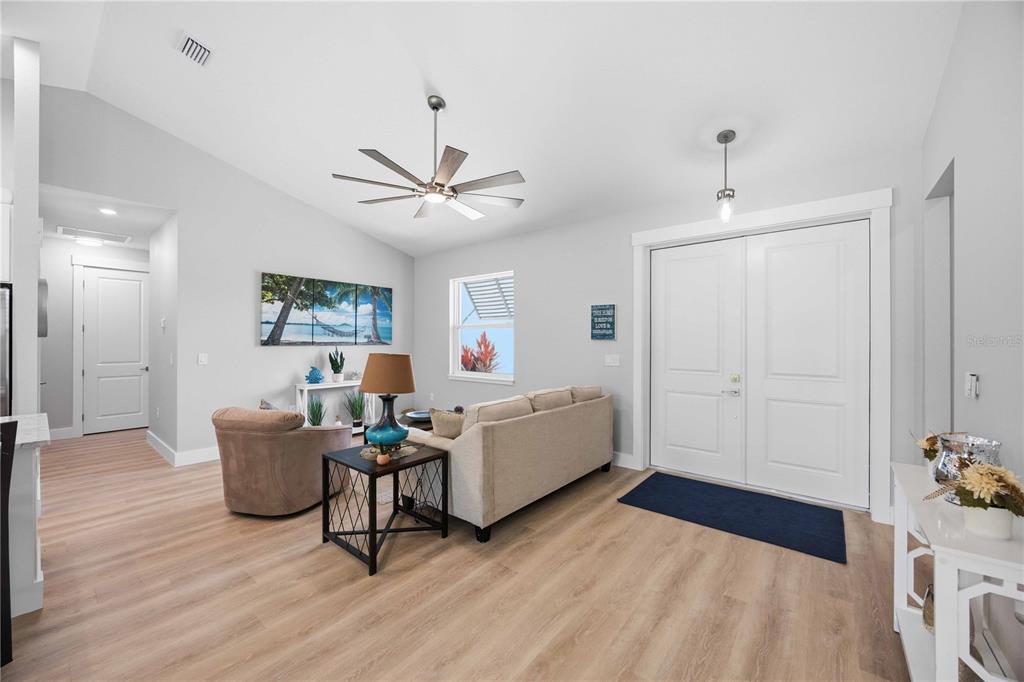 A living room features light wood flooring, a vaulted ceiling, a ceiling fan, and double doors — 10443 RIVERSIDE ROAD, PORT CHARLOTTE, FL