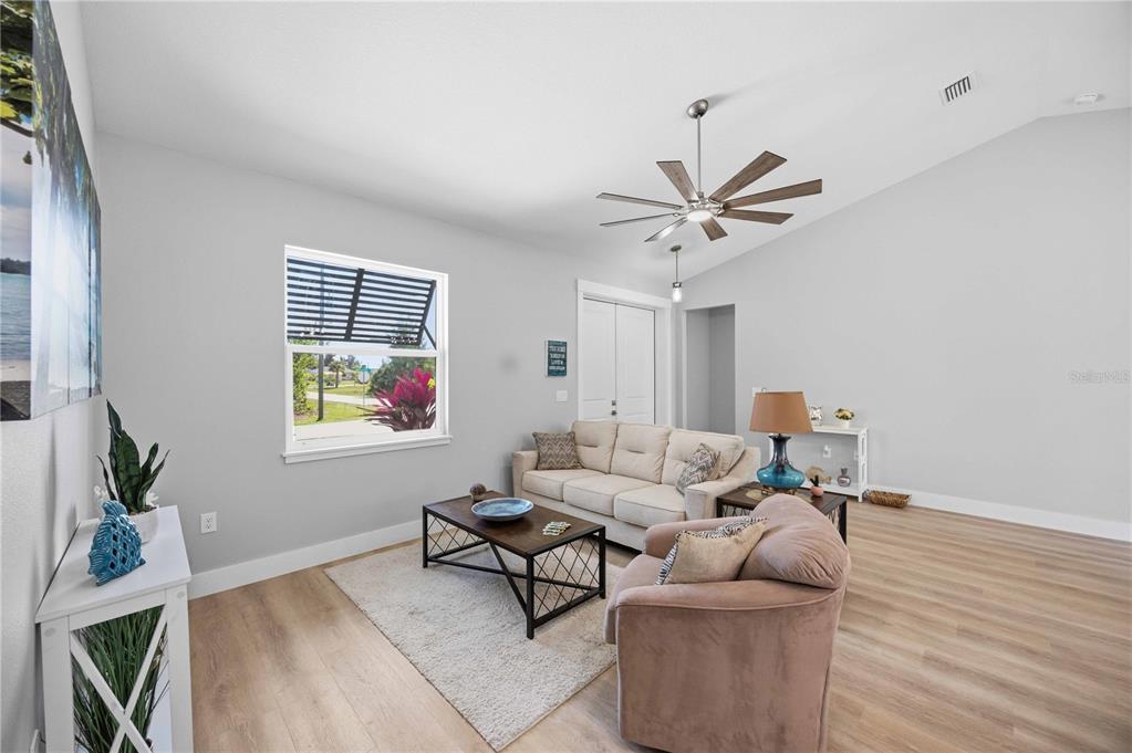 A living room features light wood-look flooring, a beige sofa, and a vaulted ceiling — 10443 RIVERSIDE ROAD, PORT CHARLOTTE, FL
