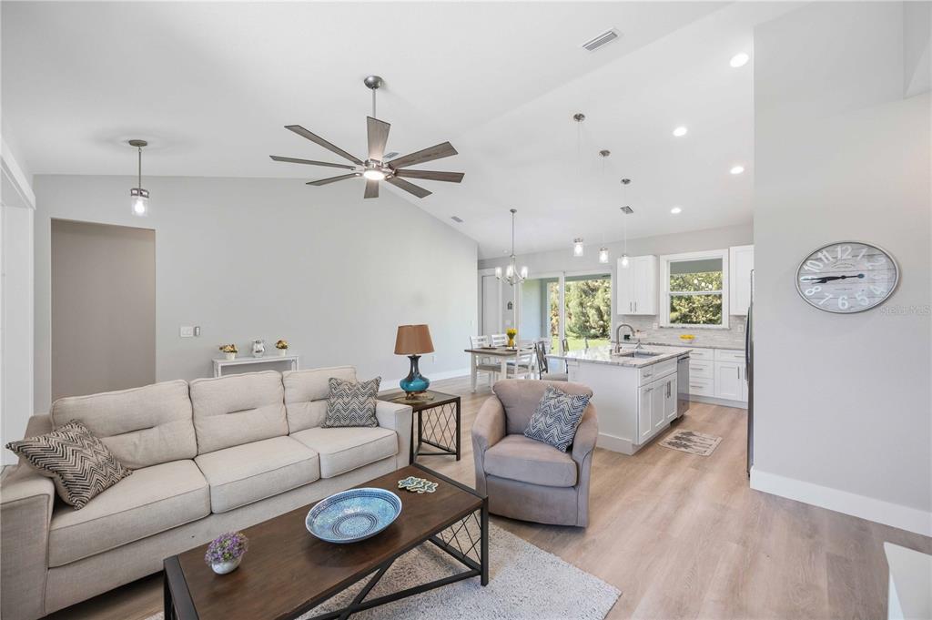 An open-concept living room and kitchen feature light wood flooring, white cabinets, and vaulted ceilings — 10443 RIVERSIDE ROAD, PORT CHARLOTTE, FL