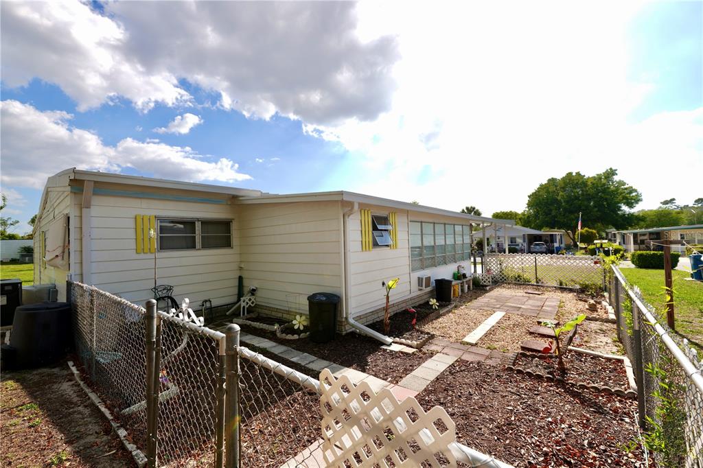 The exterior of a single-story mobile home features light-colored siding, a fenced yard, and landscaping — 7338 THORPP AVENUE, BROOKSVILLE, FL