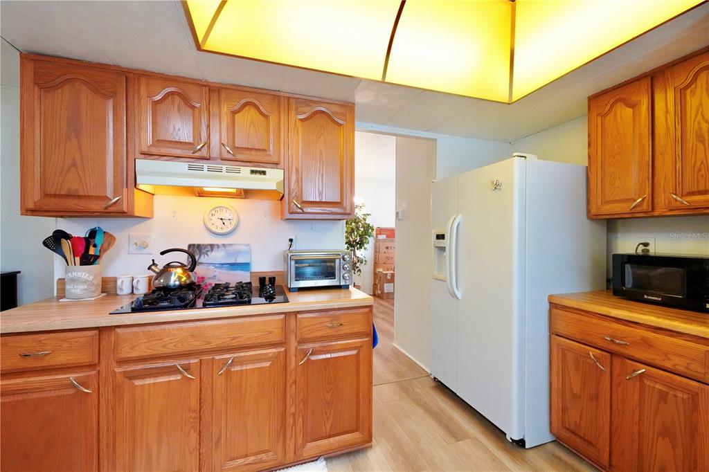 A kitchen features wood cabinets, a white refrigerator, and a gas cooktop under a light — 7338 THORPP AVENUE, BROOKSVILLE, FL