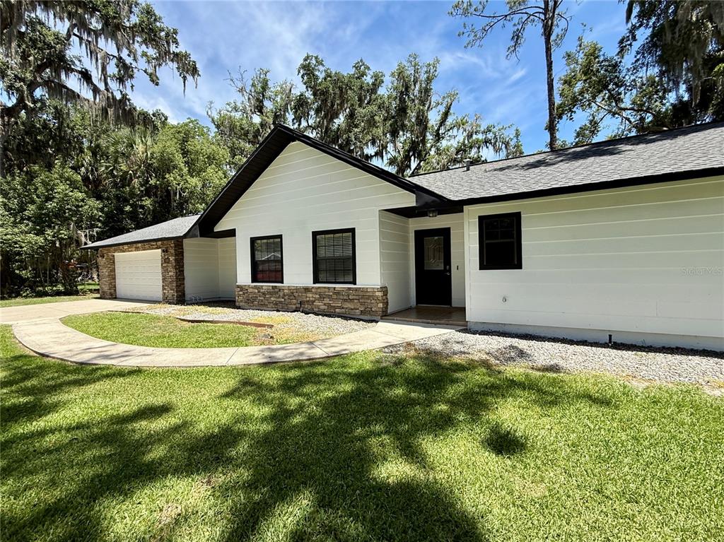 A white house with black trim, a stone accent wall, and a concrete walkway — 645 SE 21ST PLACE, OCALA, FL