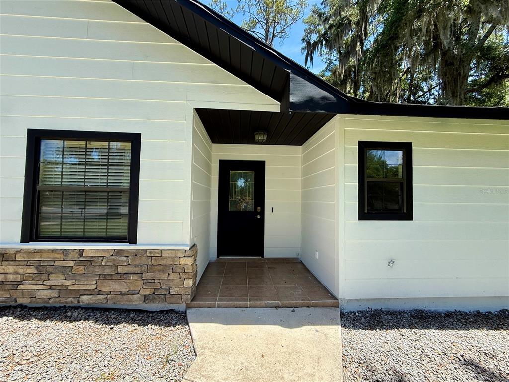 The exterior of a house features white horizontal siding, stone accents, and a black door — 645 SE 21ST PLACE, OCALA, FL
