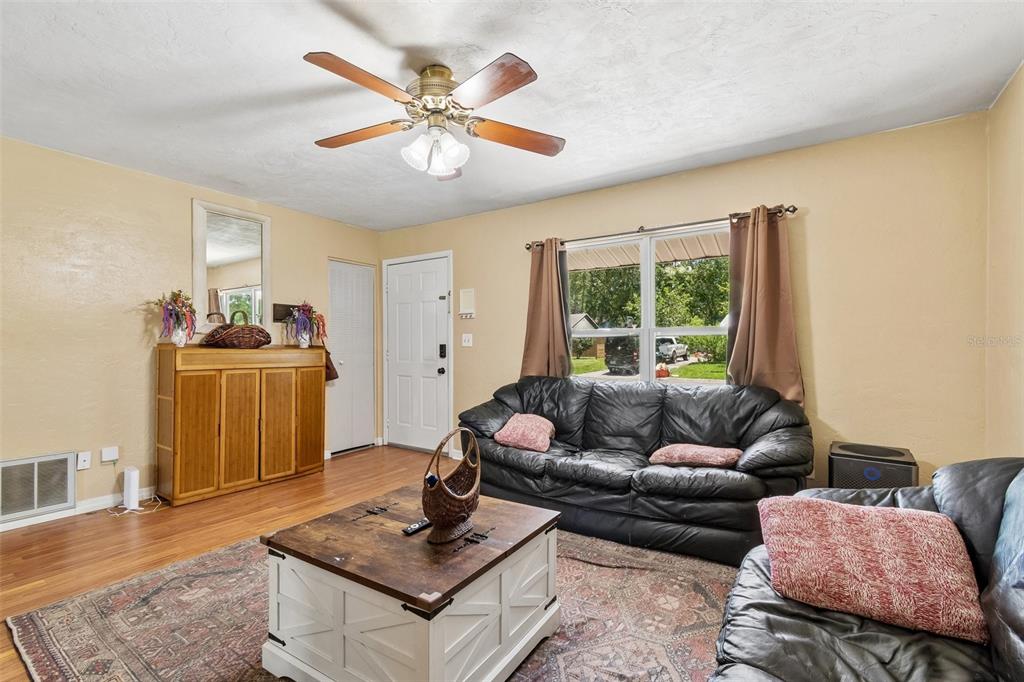 A living room features wood flooring, a ceiling fan, a black sofa, and a coffee table — 5934 NW 30TH TERRACE, GAINESVILLE, FL