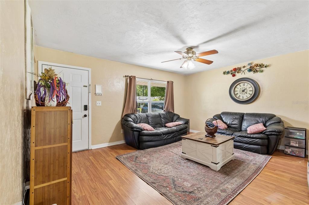 A living room features wood-look flooring, two black leather sofas, a coffee table, and a rug — 5934 NW 30TH TERRACE, GAINESVILLE, FL