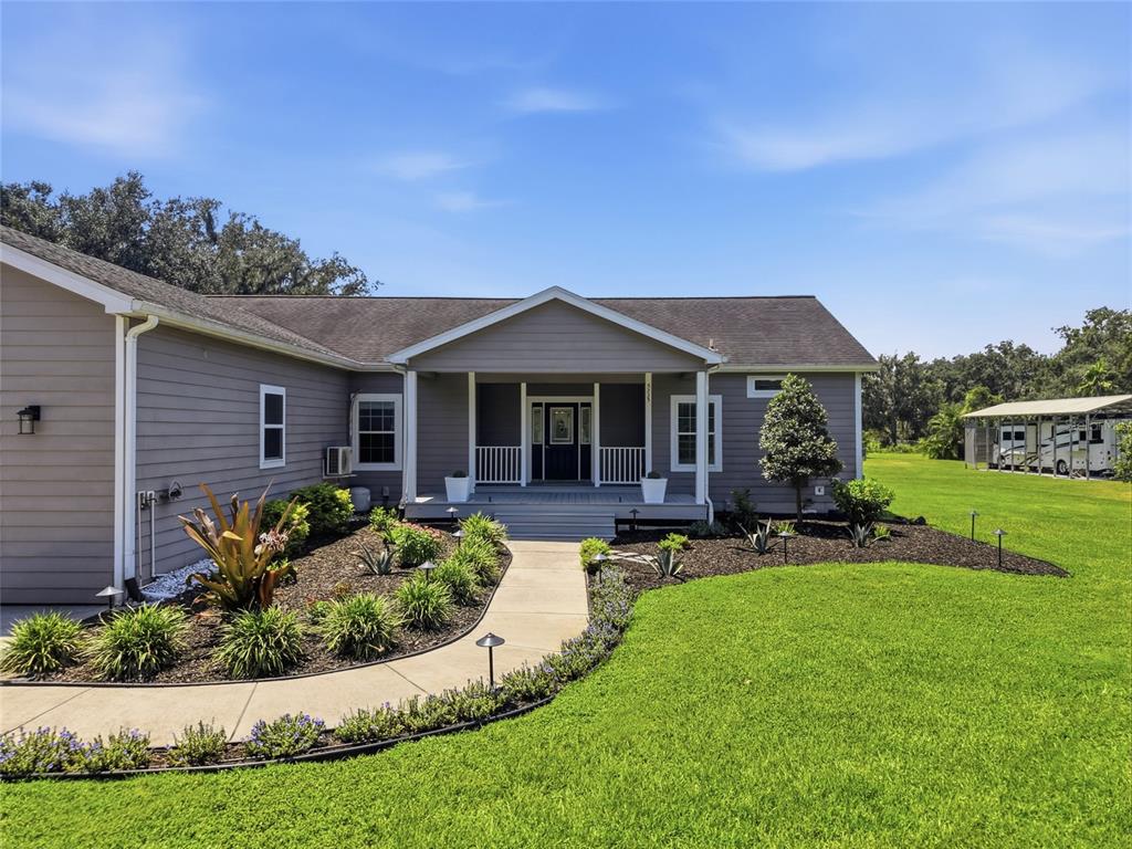 A gray single-story house features a covered front porch, a concrete walkway, and landscaped beds — 5335 SHAKESPEARE DRIVE, DOVER, FL