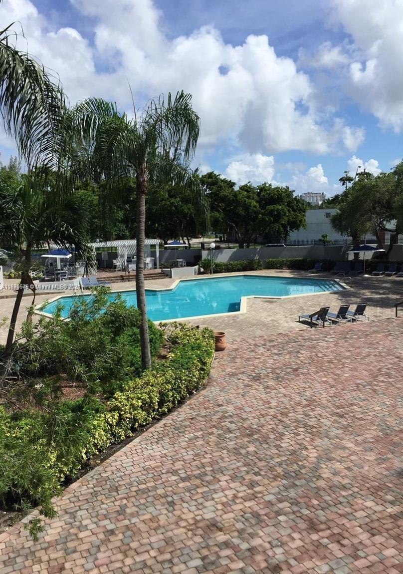 A swimming pool with a brick patio and palm trees under a cloudy blue sky — 1470 NE 123rd St # A902, North Miami FL 33161, NORTH MIAMI, FL
